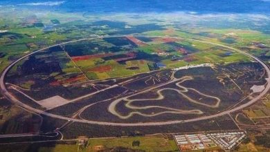 Vista aerea del progetto dell'autodromo NTC-Porsche in Puglia, con una pista principale ovale e percorsi interni complessi, circondati da campi agricoli.