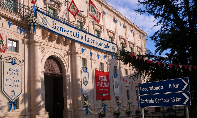 Immagine satirica del Palazzo Ducale di Martina Franca con la scritta Benvenuti a Locorotondo, stendardi della Festa dell'Unità e cartelli per Locorotondo e Capitolo